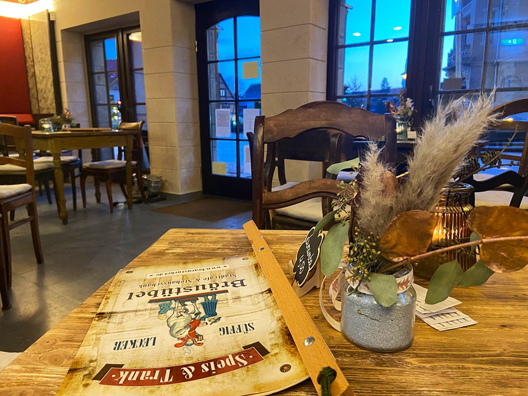 Stilleben, Tisch mit Gebinde und Speisekarte am Holzbügel